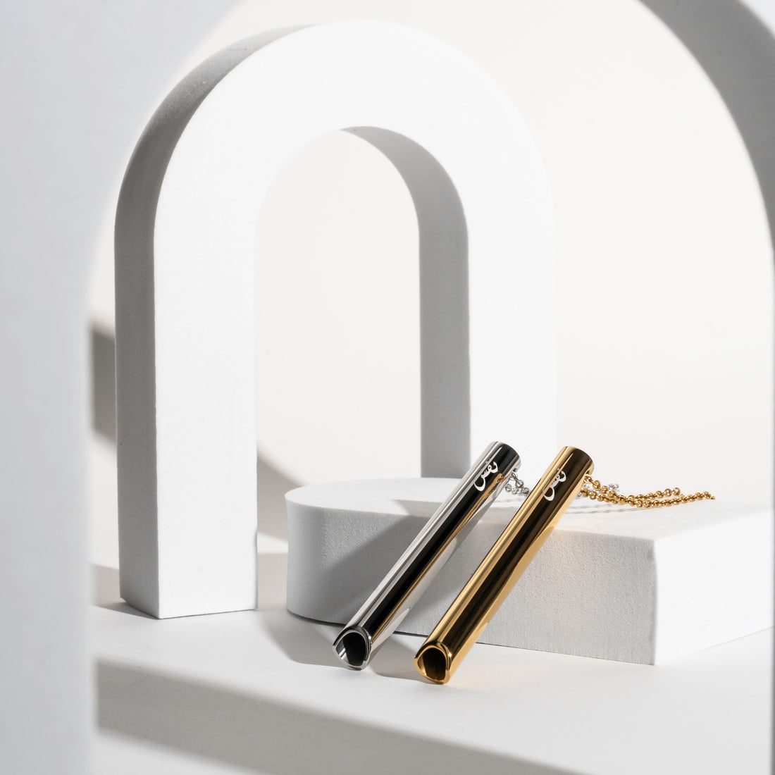 Two Nafas breathing pendants in gold and silver resting on a pale plaster form